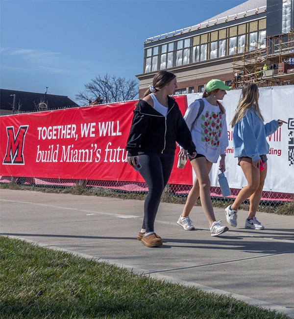students walking on campus in front of a construction fence that says "Together, We will build Miami's future"